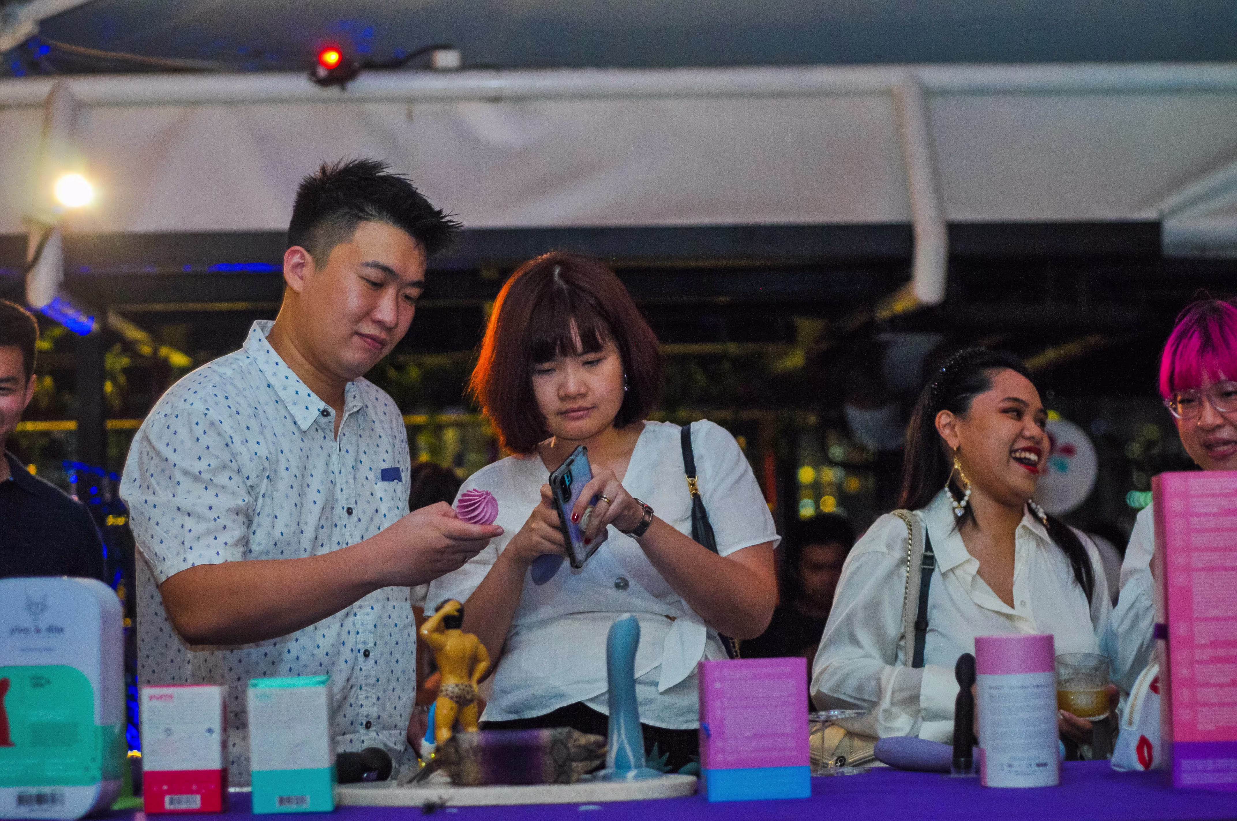 A group of attendees exploring and viewing intimate wellness products on the display table at the Teman Asmara Bersua anniversary event