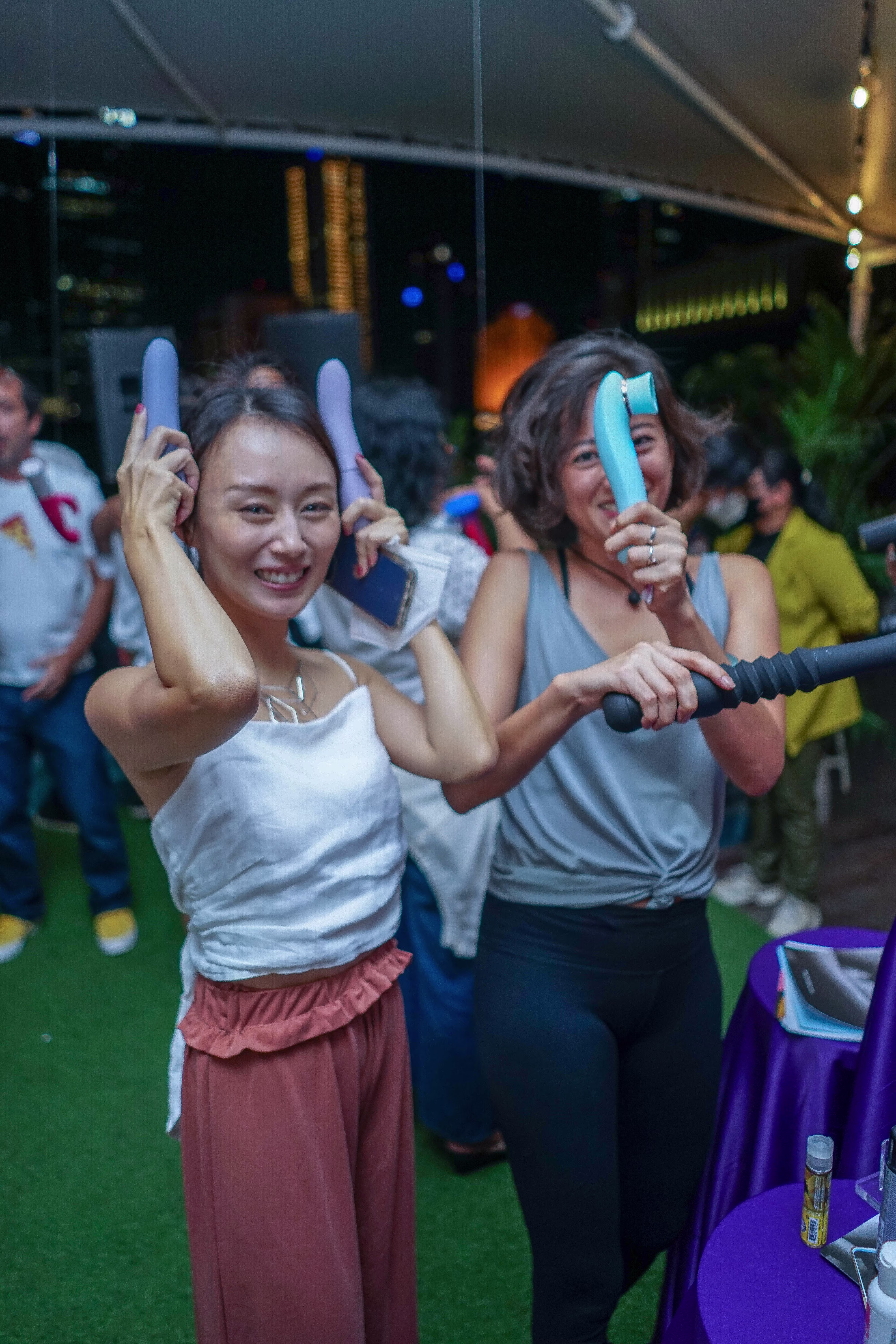 Two playful female guests holding vibrators up to their heads like bunny ears at the Laciasmara 7th anniversary celebration