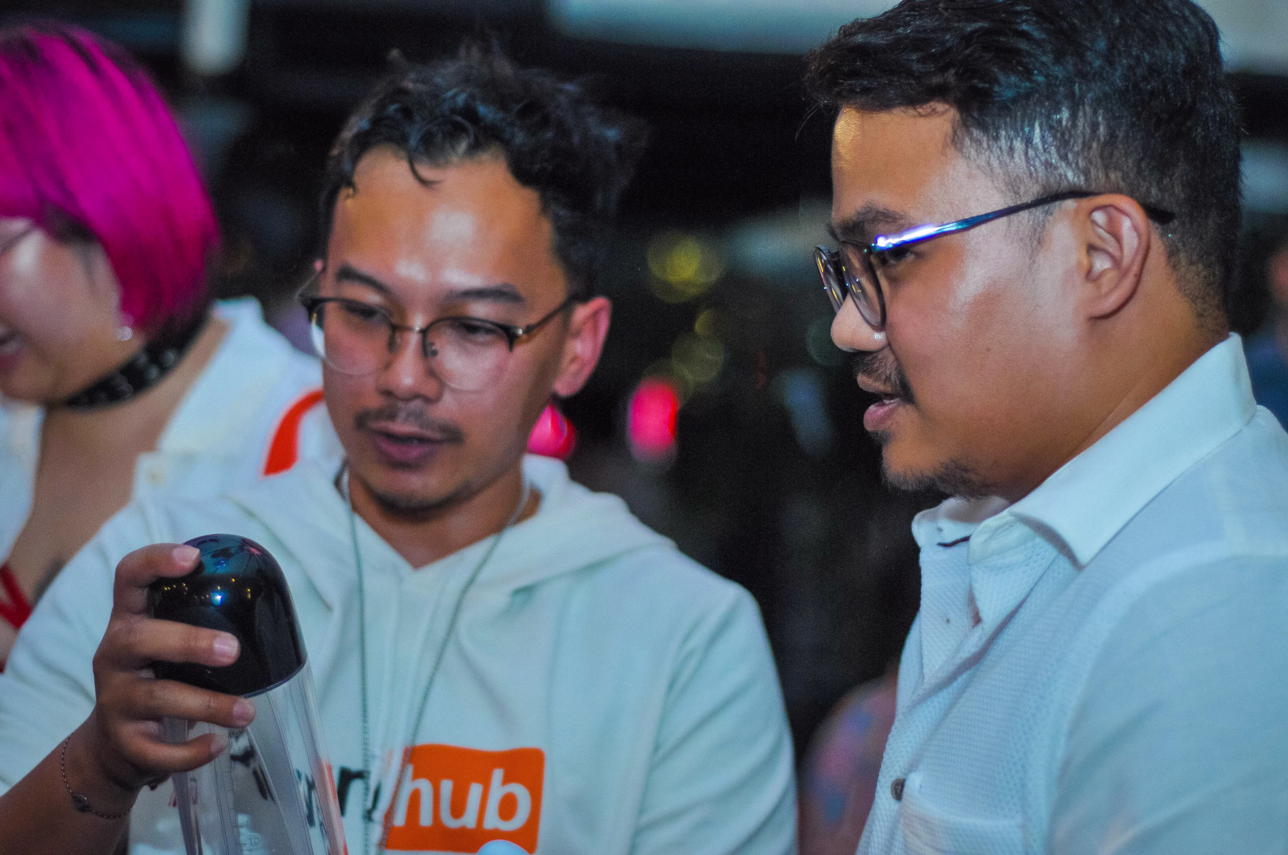 Two men viewing the product display, with one examining a Vedo penis pump at the Teman Asmara Bersua gathering