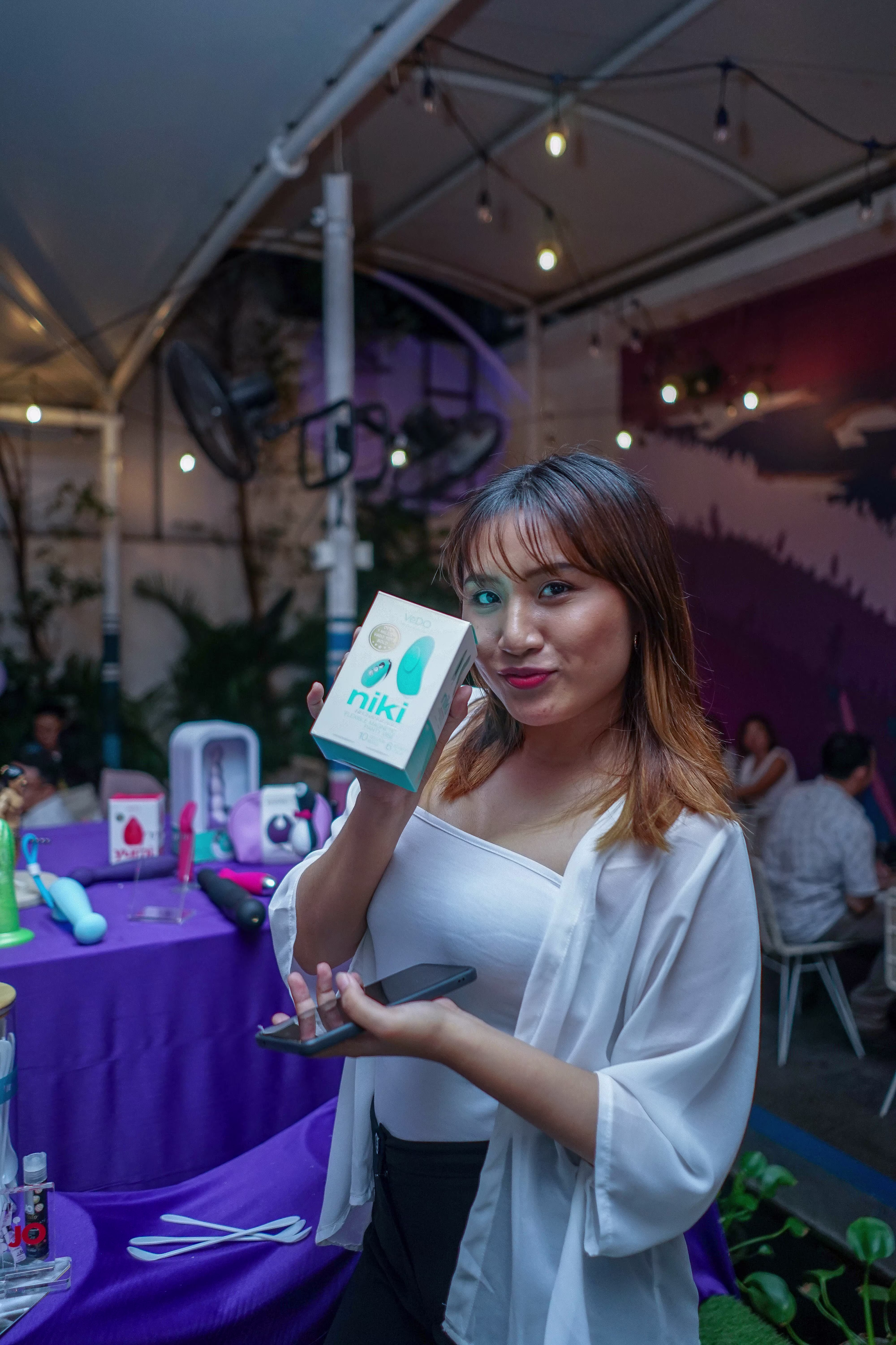 A guest posing expressively while showcasing a sleek sexual wellness vibrator at the Teman Asmara Bersua party
