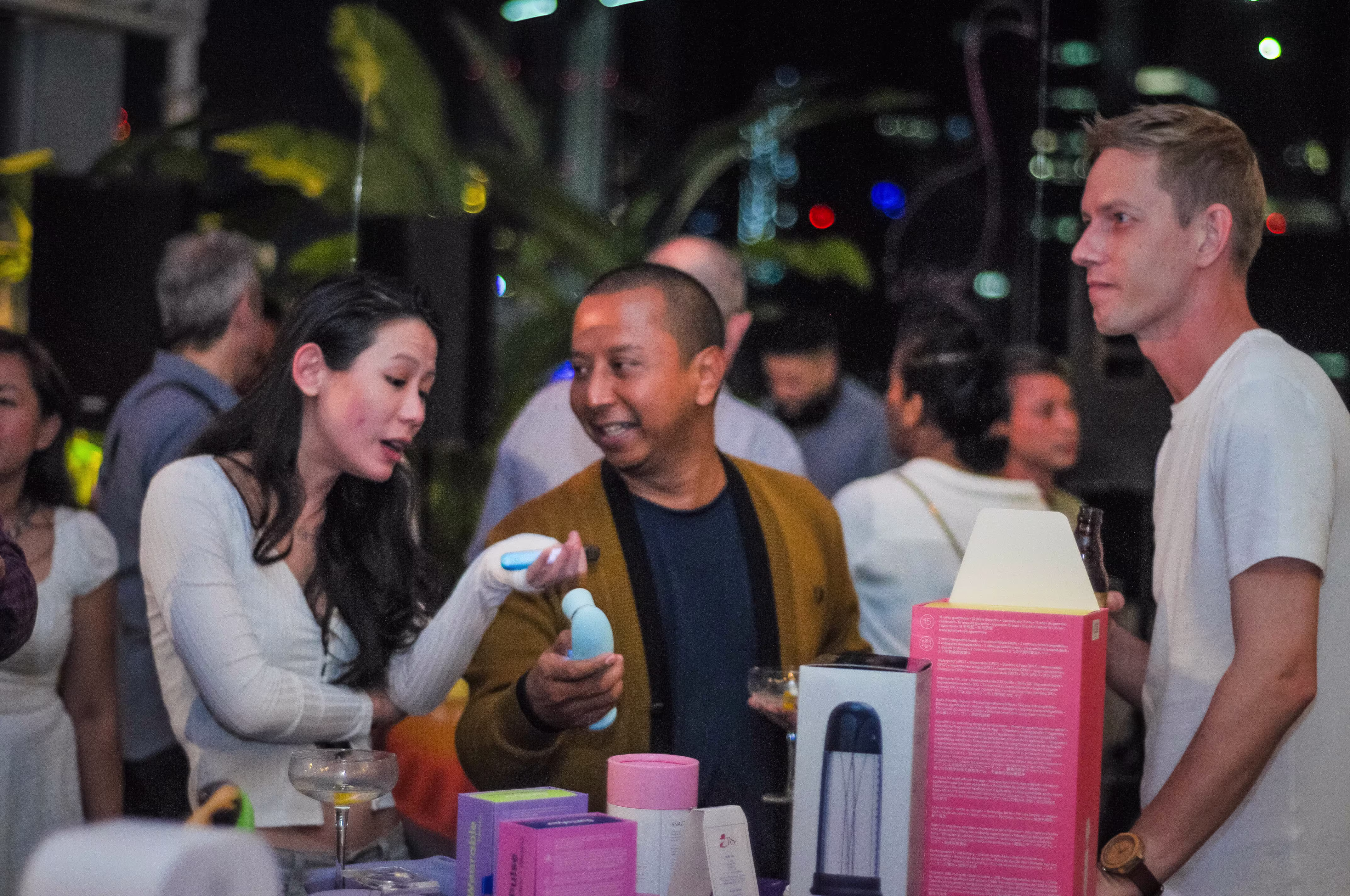 A group of three attendees discussing the features and design of a modern clitoral suction vibrator at ¡Porqué No!