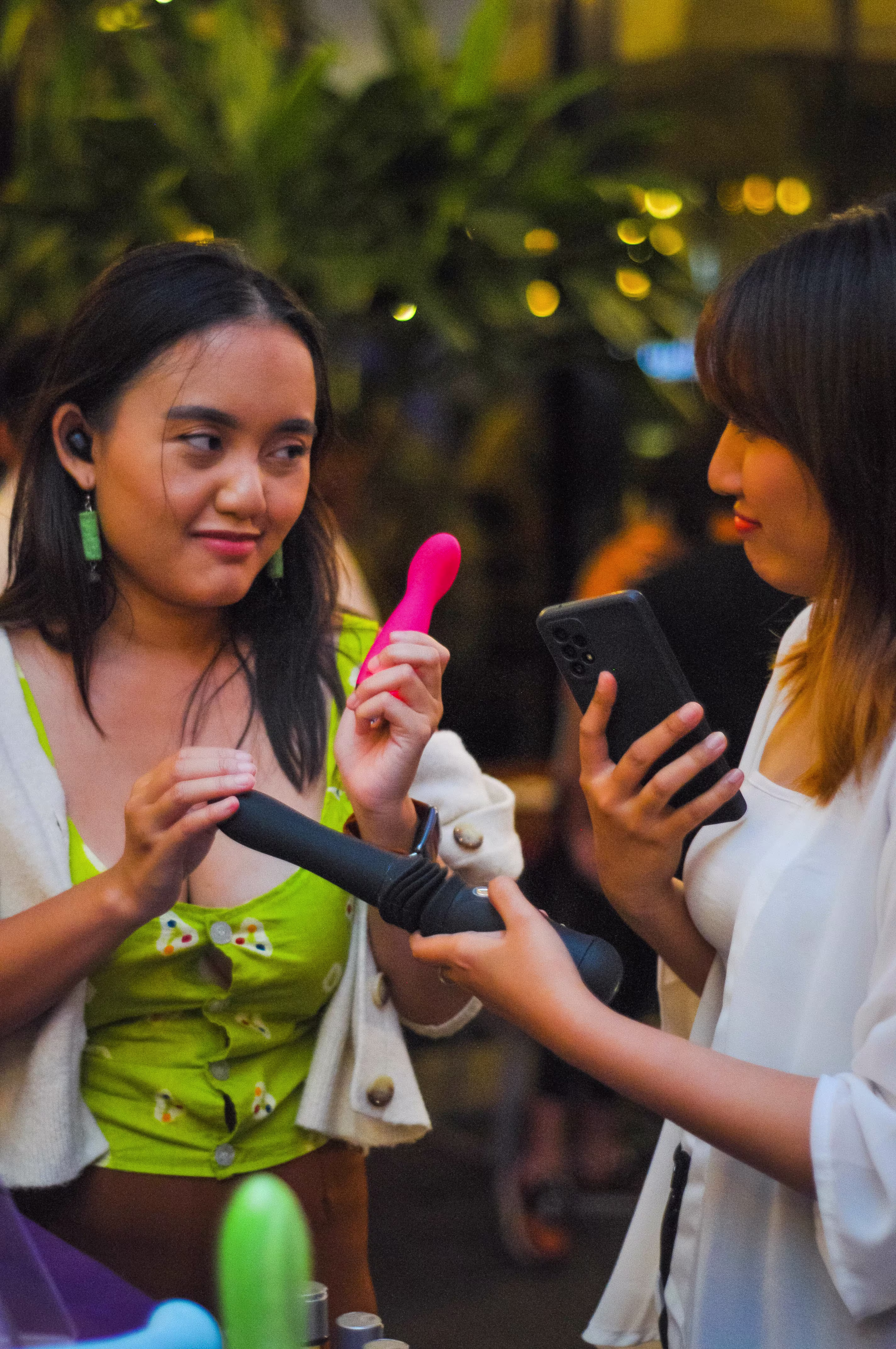 Two female attendees holding and examining educational adult dildo models at the Laciasmara community gathering