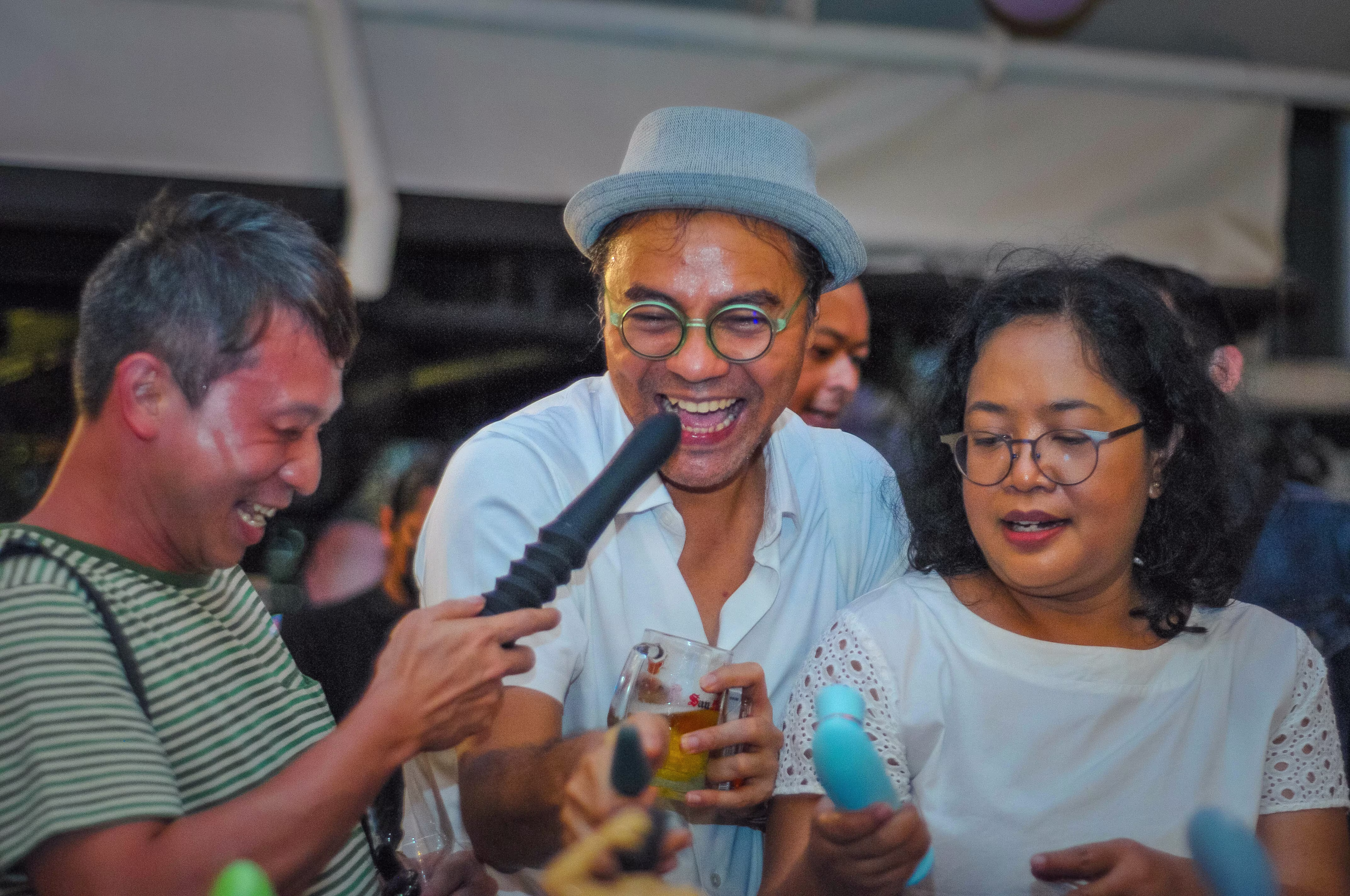 Three party guests laughing and sharing a playful moment while handling an educational adult novelty model