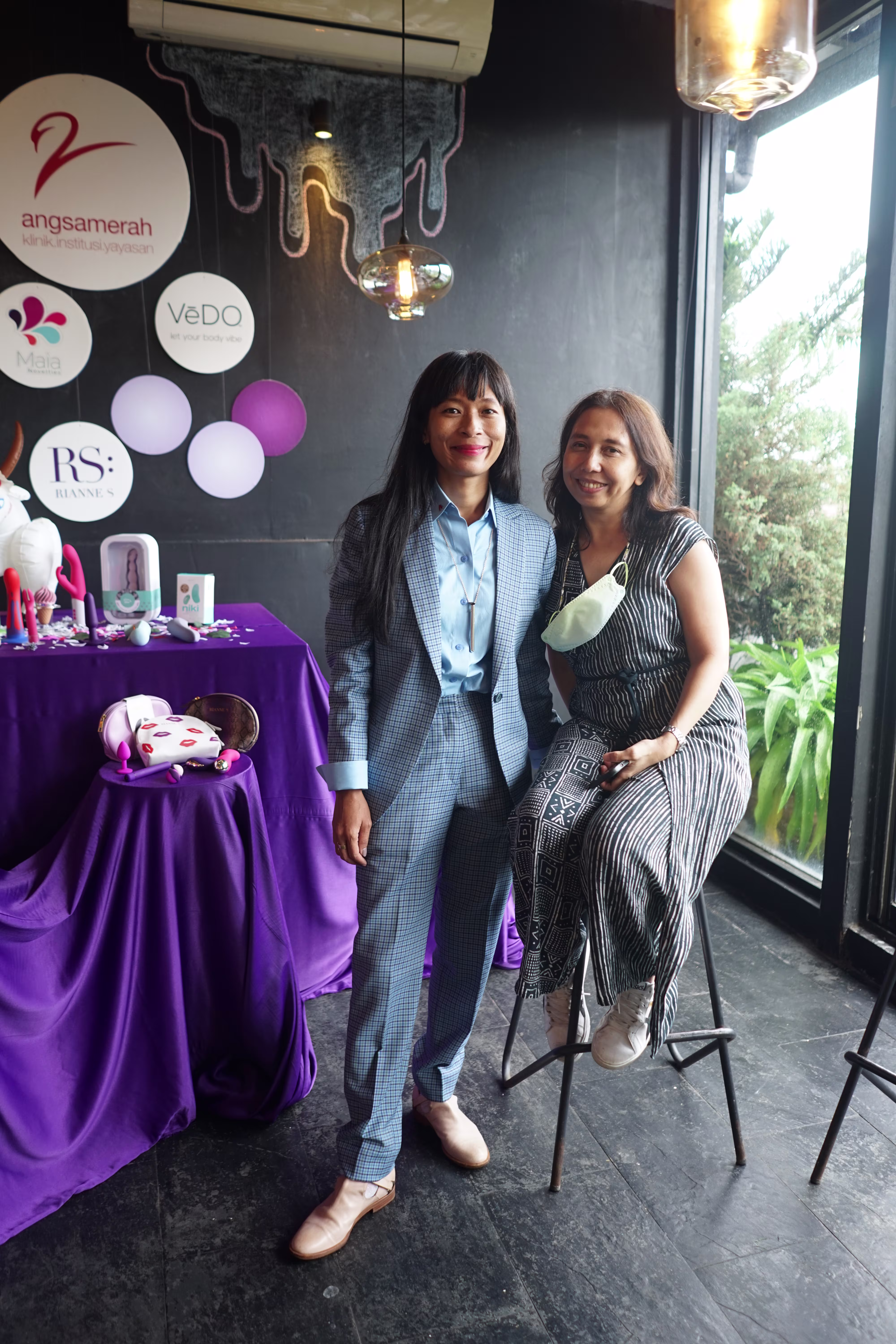 Laciasmara founder Rendra Susanti standing and smiling alongside a seated female guest next to the professional medical and wellness product display