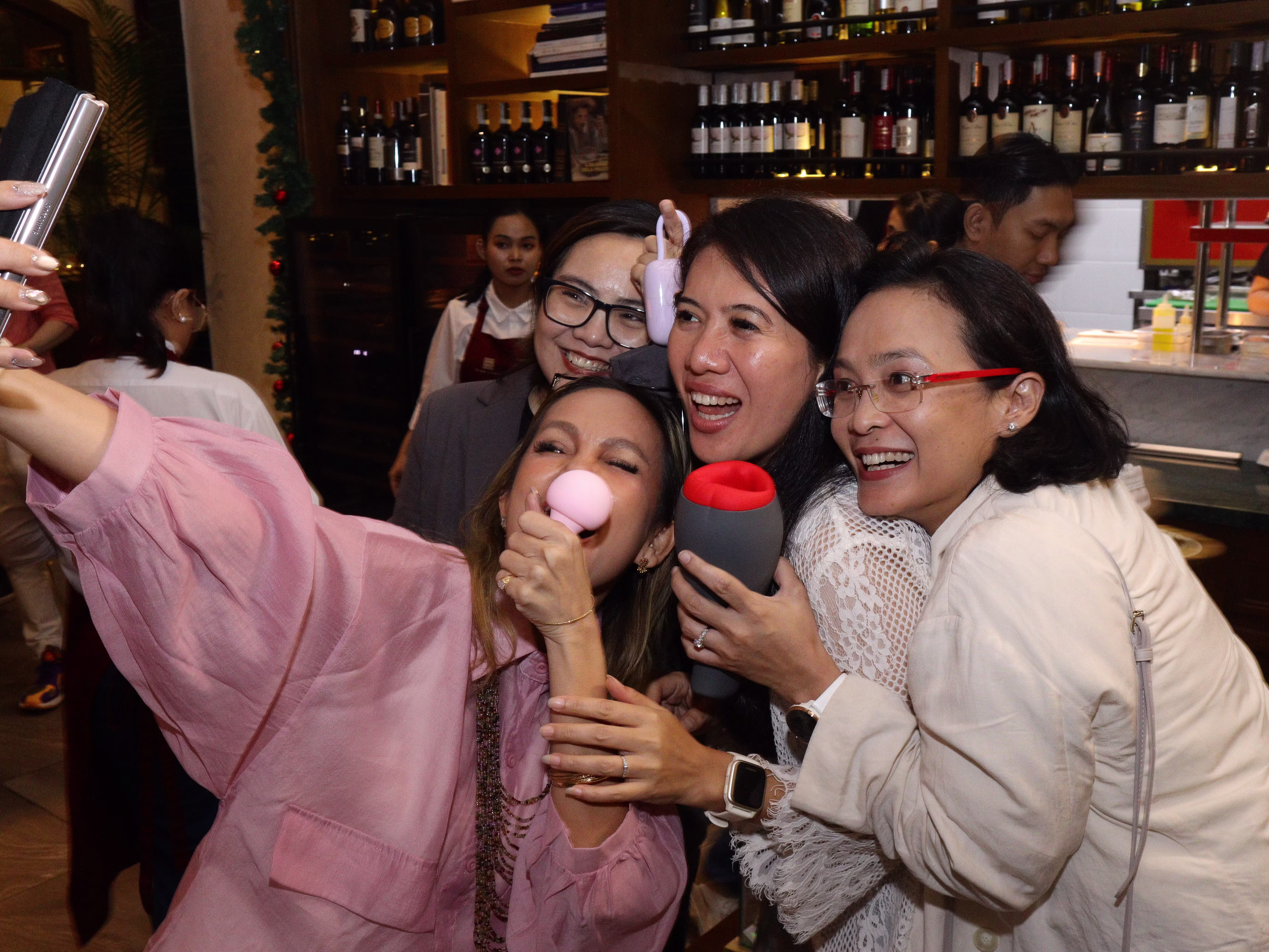 A person taking a selfie with three others while holding a sex toys at the Dasa Asmara Bersua event.