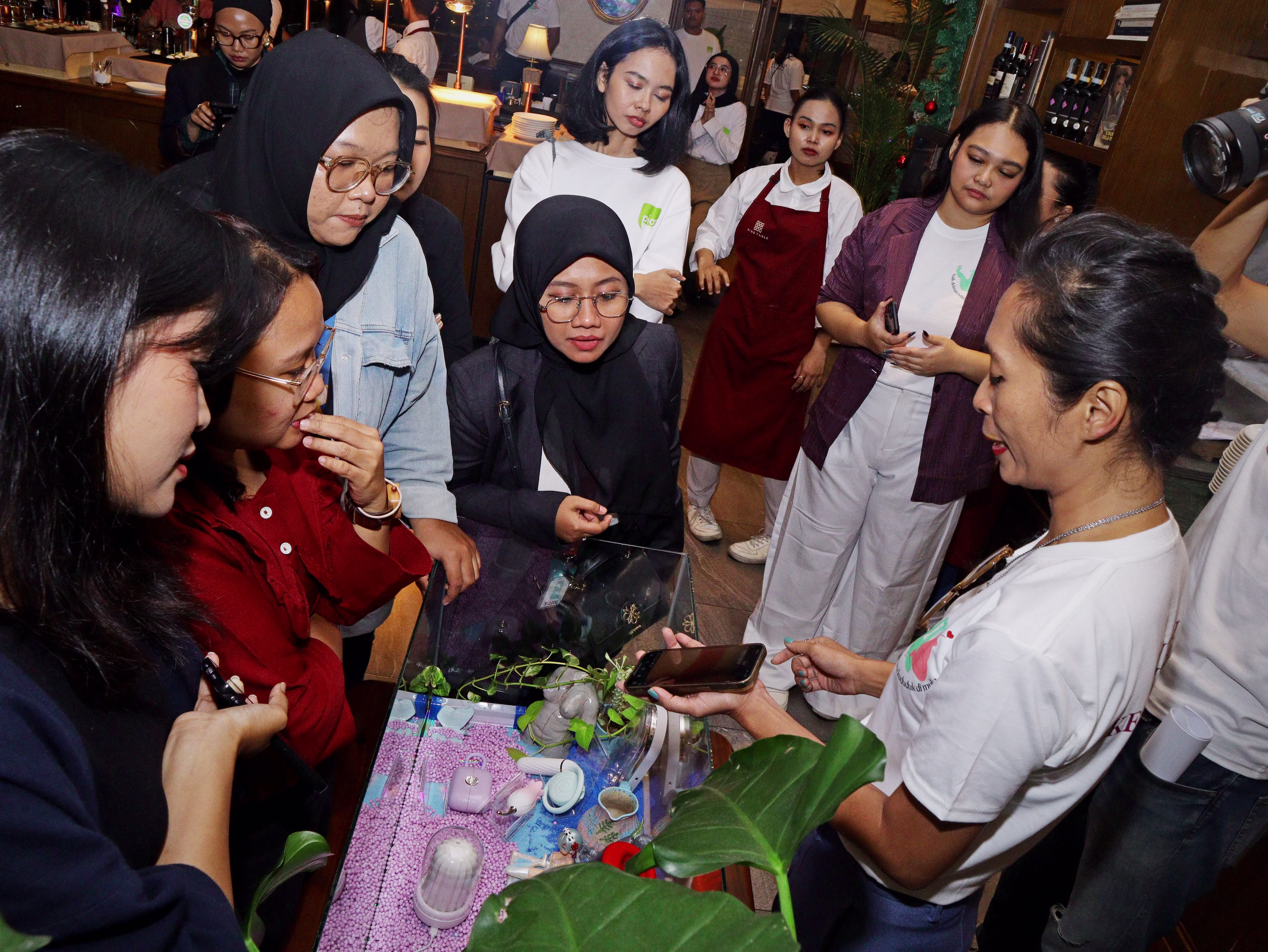 Rendra Susanti explaining at a product display, showing and explaining various sex toys to an engaged audience of guests.